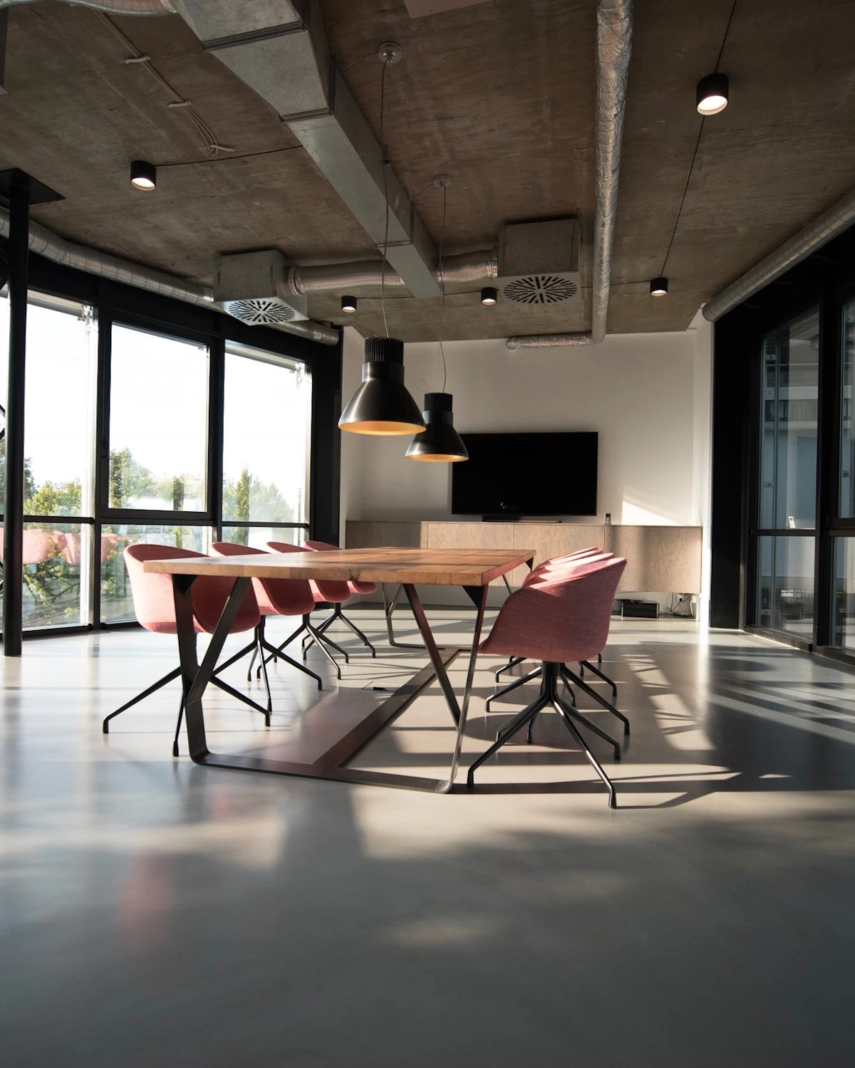 A sunlit modern meeting room with a long table and floor-to-ceiling windows